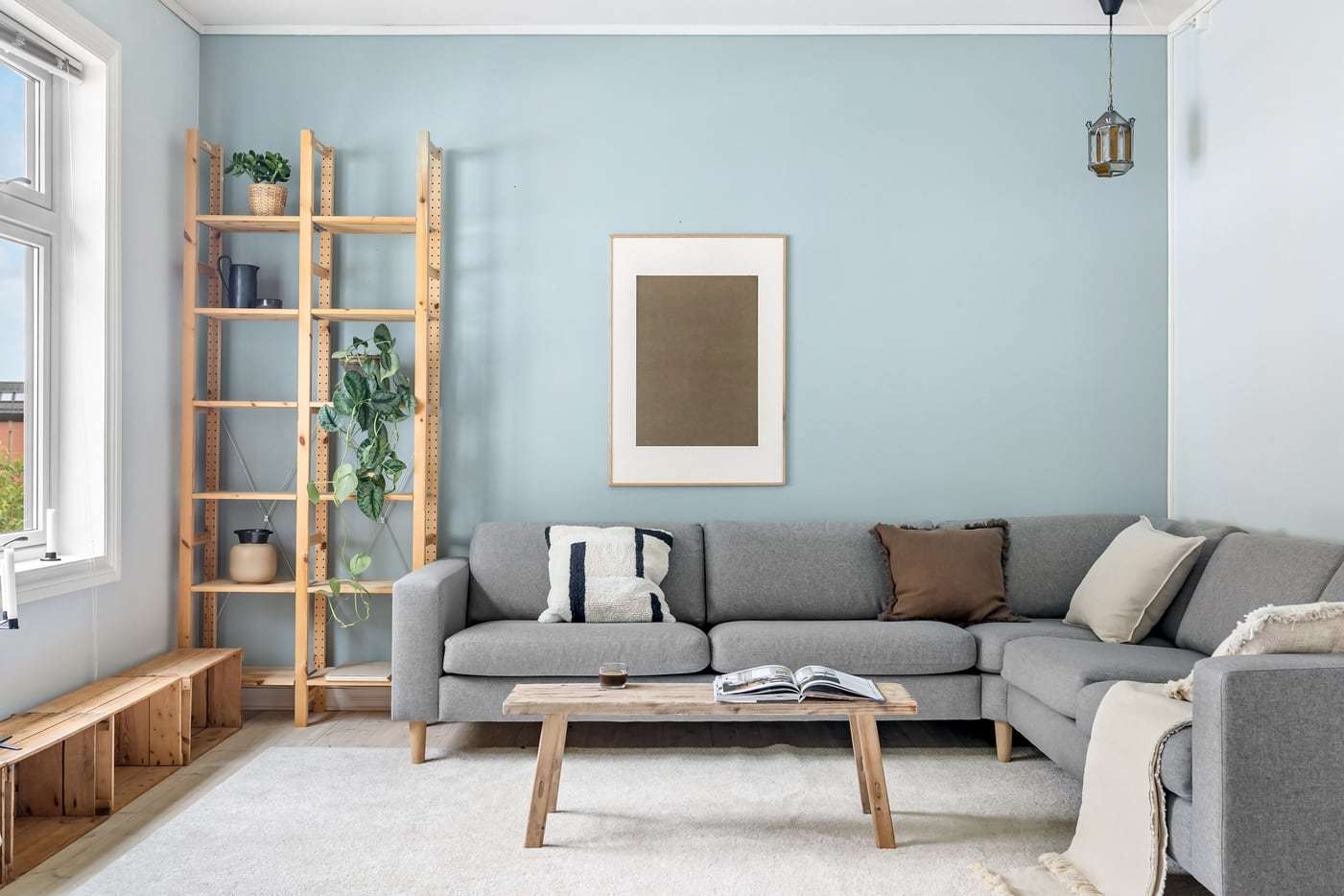 Wohnzimmer mit grauem Ecksofa, Holztisch, Regal und hellblauer Wand
